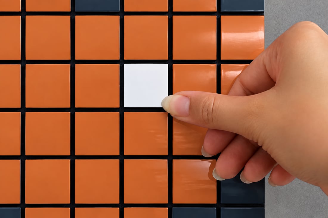 Une main clipse une tesselle blanche au milieu d'une composition orange et bleue